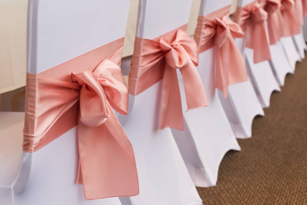 A row of reception chairs with pink satin sashes at a wedding