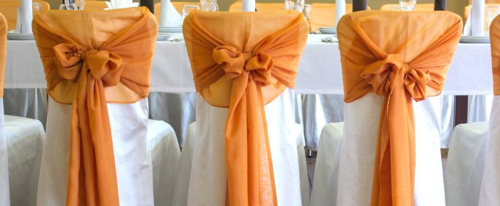 A row of three chairs with deep orange sashes at an Autumn wedding