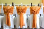 A row of three chairs with deep orange sashes at an Autumn wedding