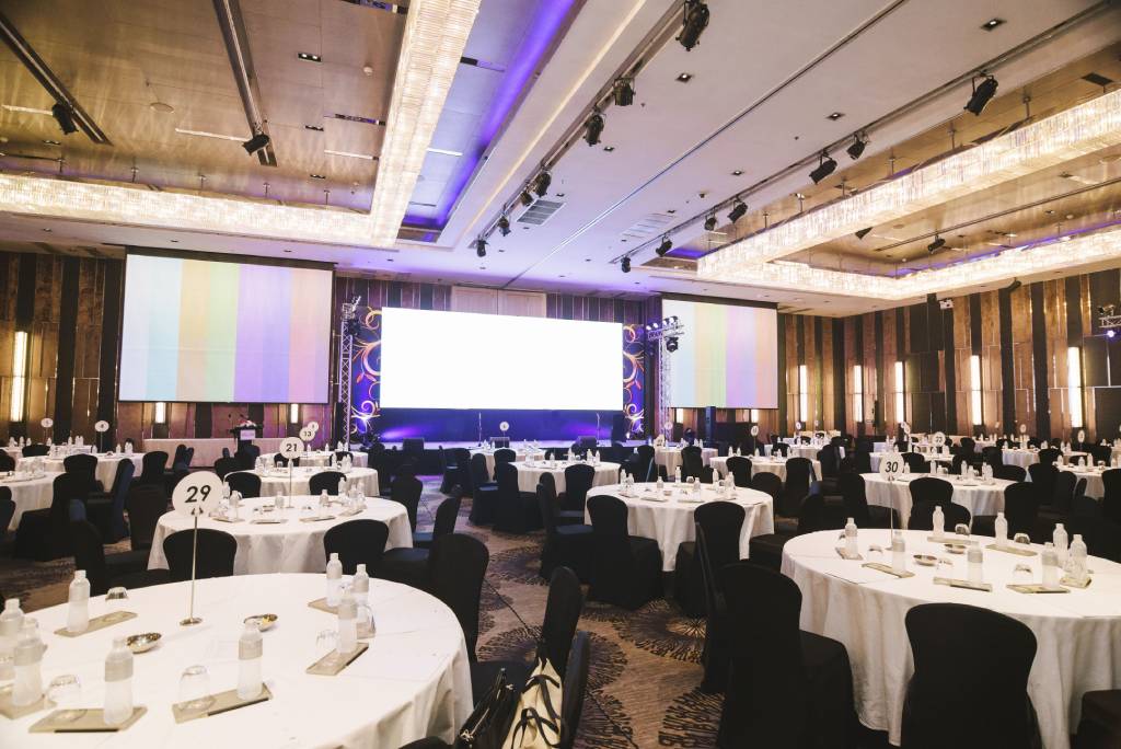 Tables set up in front of a large projection screen at a formal corporate event