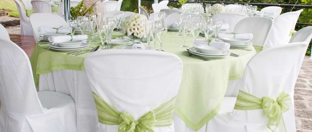 A beautiful table setting at a wedding with green sashes on the chairs