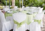 A beautiful table setting at a wedding with green sashes on the chairs